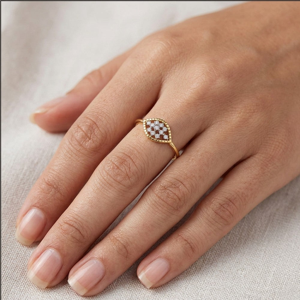 A gold ring with a marquise-shaped, worn on a woman's hand against a neutral textured fabric background.