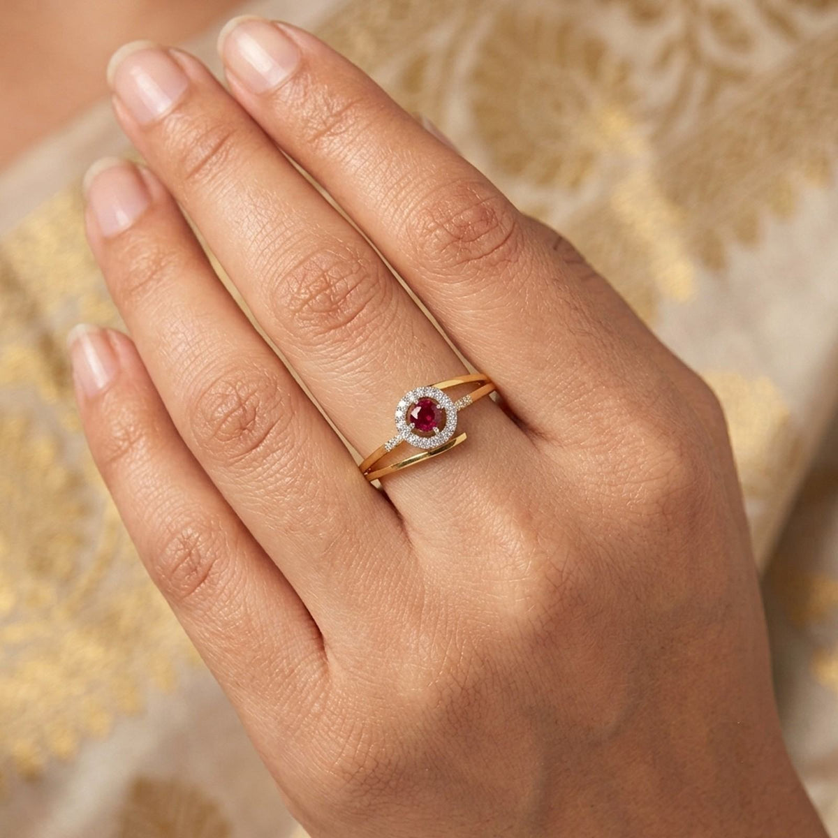 A close-up of a hand wearing a gold ring with a round red gemstone, set against a soft beige.