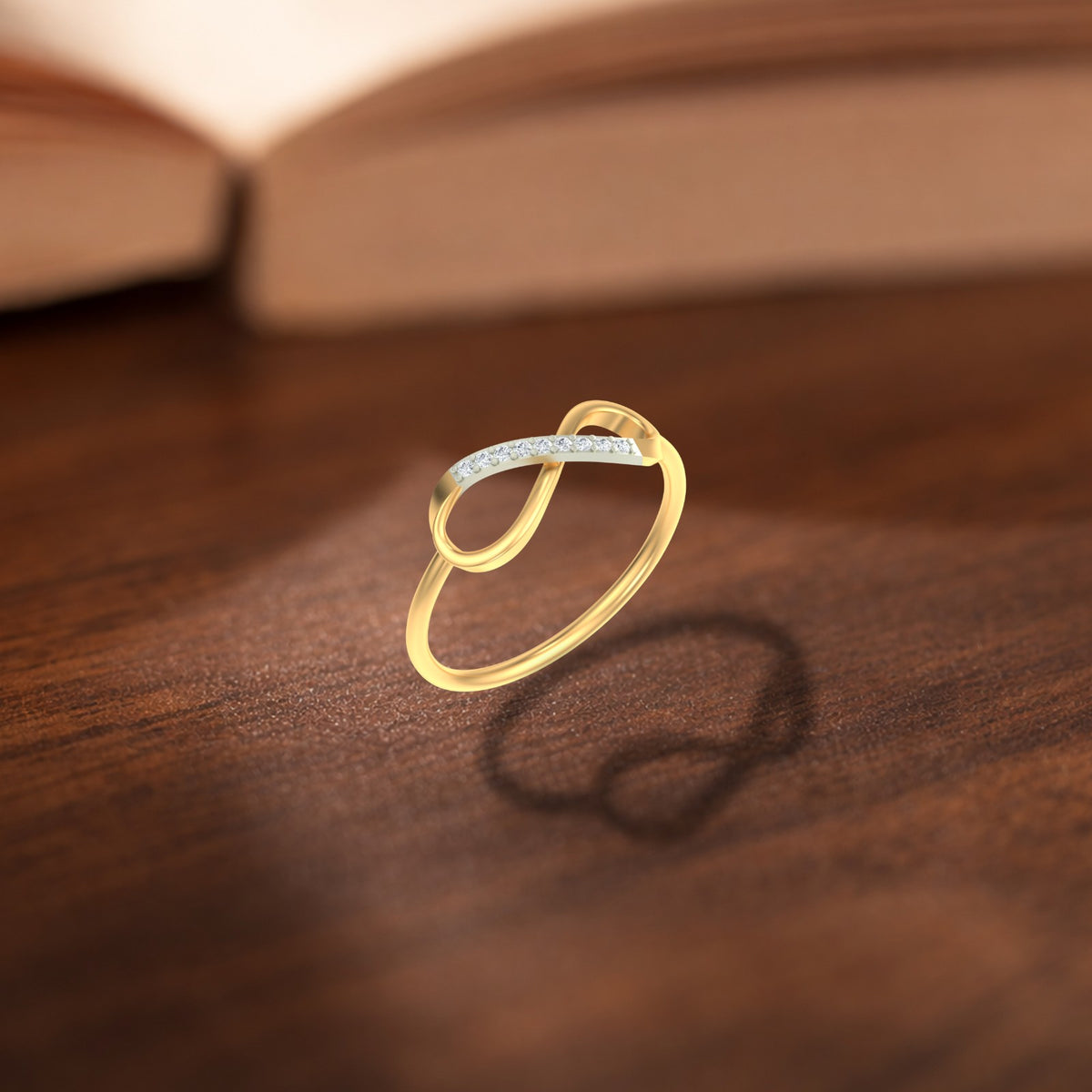 A gold and diamond infinity ring , resting on a dark wooden surface with a blurred open book in the background.