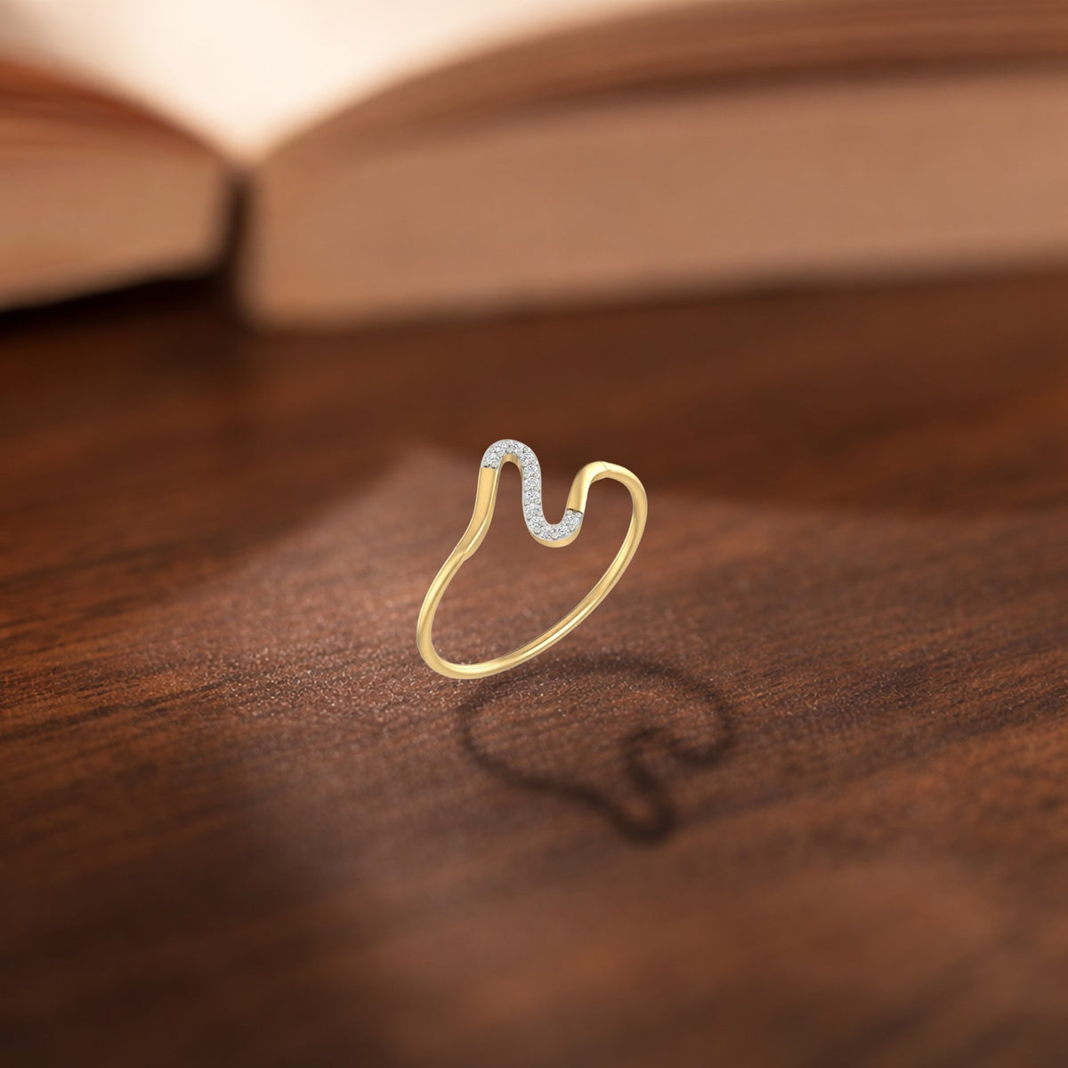A gold ring with a wavy open design, resting on a dark wooden surface.