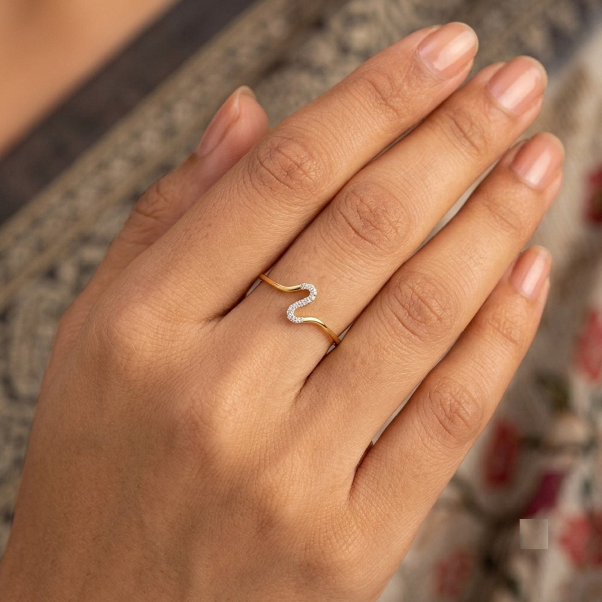 A close-up shot of a gold ring with a wavy open design, resting on a dark wooden surface.
