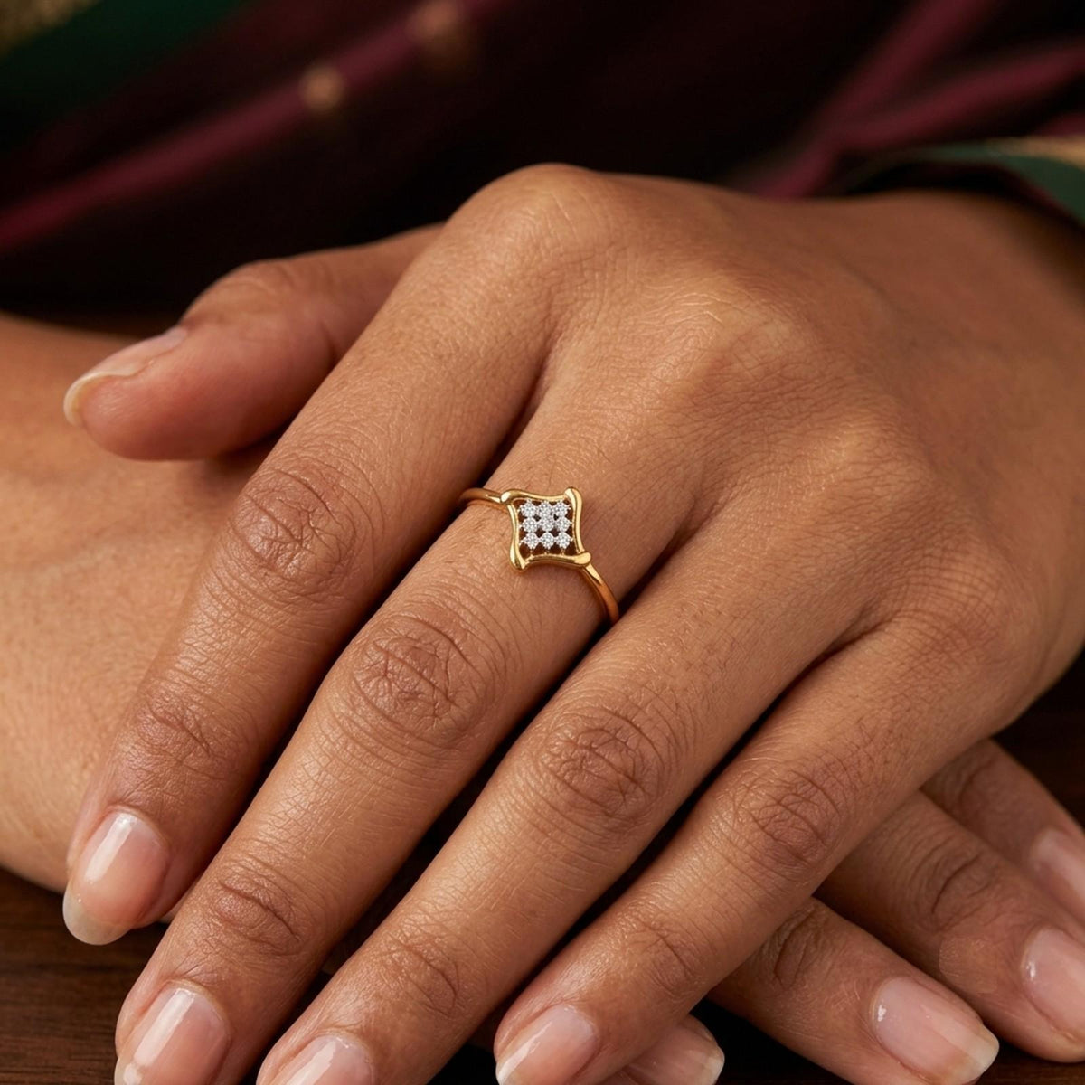 A gold ring with a small square cluster on the ring finger of a hand, shown in a close-up lifestyle shot.