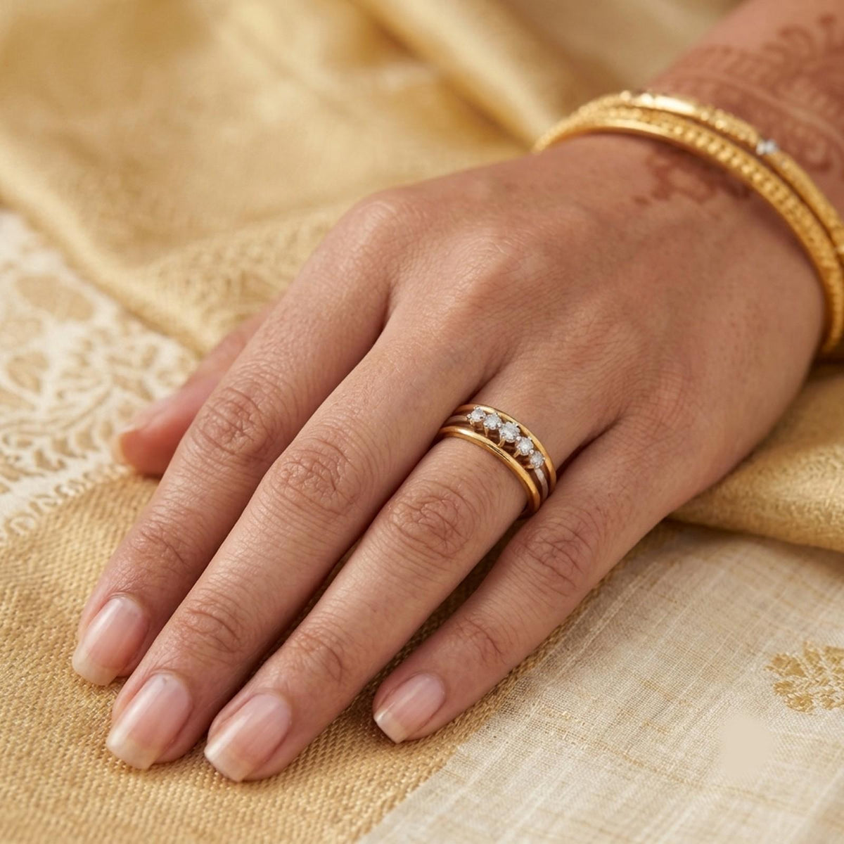 A close-up of a hand wearing a gold ring, resting on a beige patterned fabric.