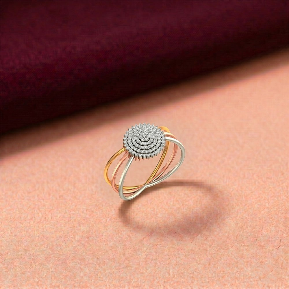A gold and diamond ring with a textured circular top, resting on a peach-colored surface with a dark burgundy background.