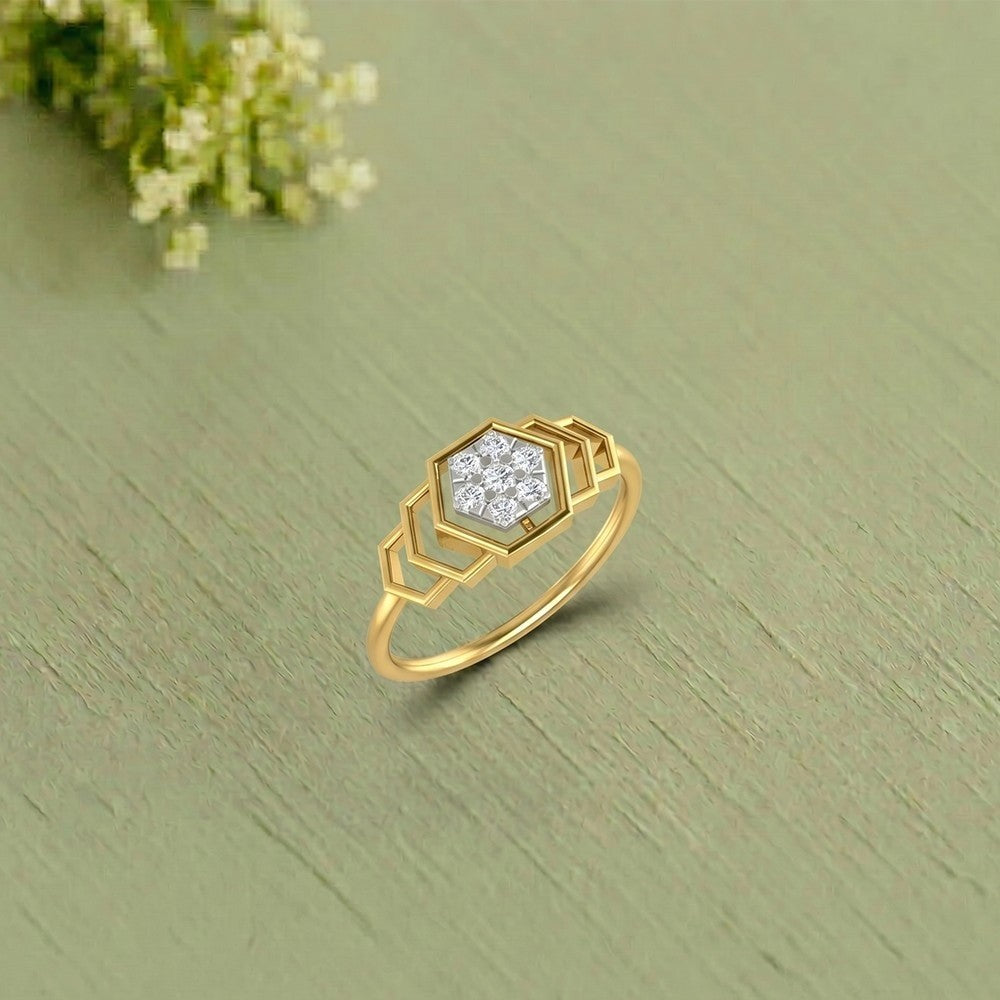 A gold ring with a geometric hexagonal setting, displayed on a textured sage green surface.