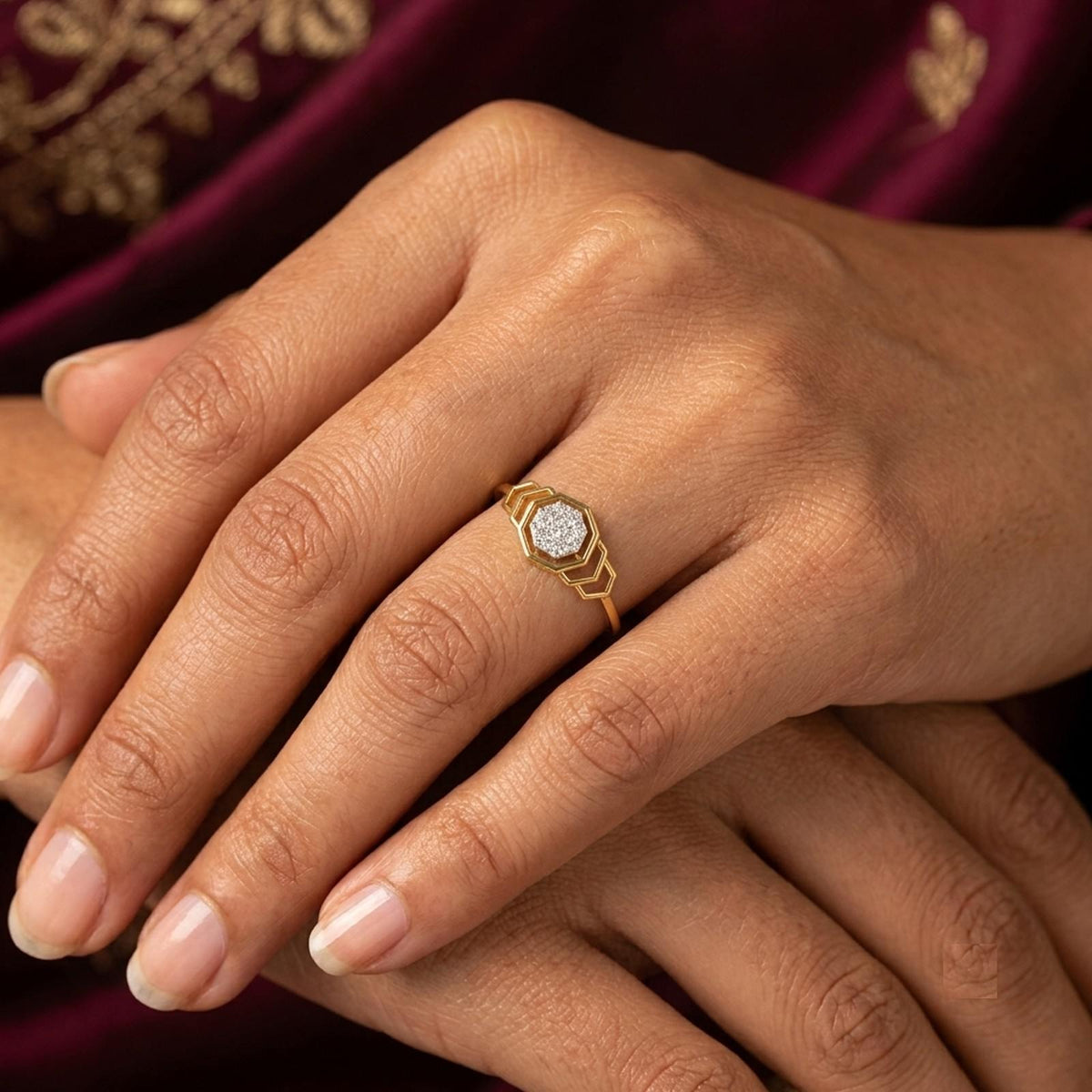 A close-up of a hand wearing a gold ring, against a dark plum fabric background.