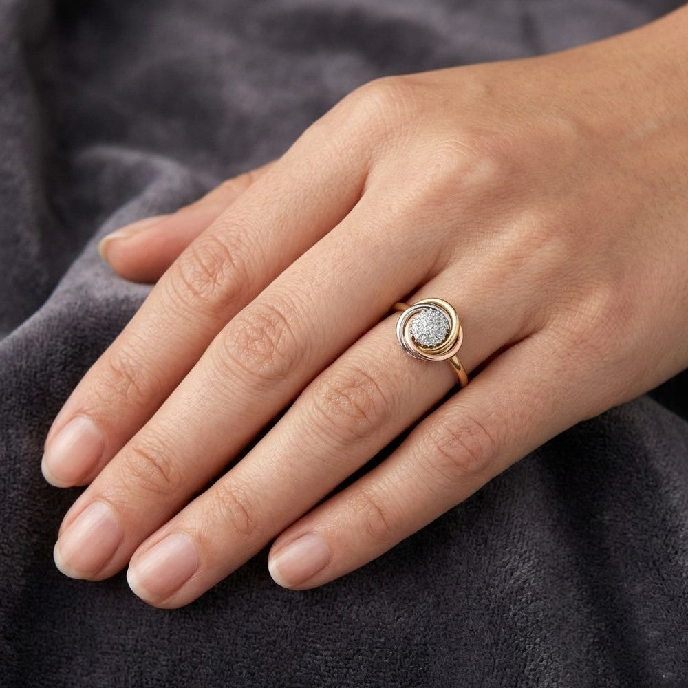 A close-up of a hand wearing a gold ring with a textured, silver-toned oval stone, resting on a dark gray fabric background.