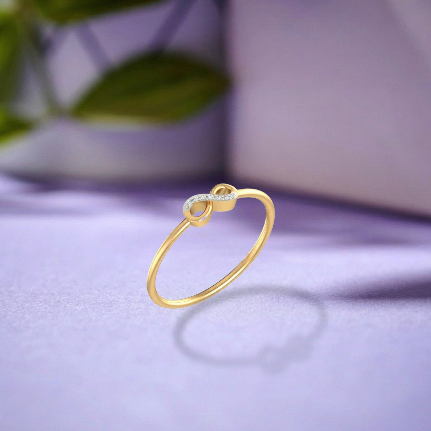 A gold and diamond infinity ring, on a dark purple surface.