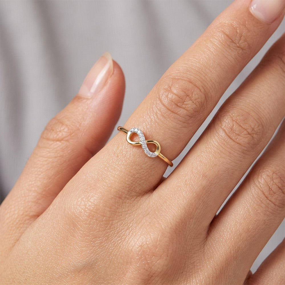 A close-up of a hand wearing a delicate infinity ring. 