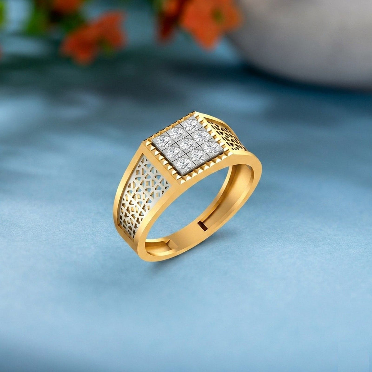 A gold ring with a square diamond cluster center and textured side, displayed on a soft blue surface.