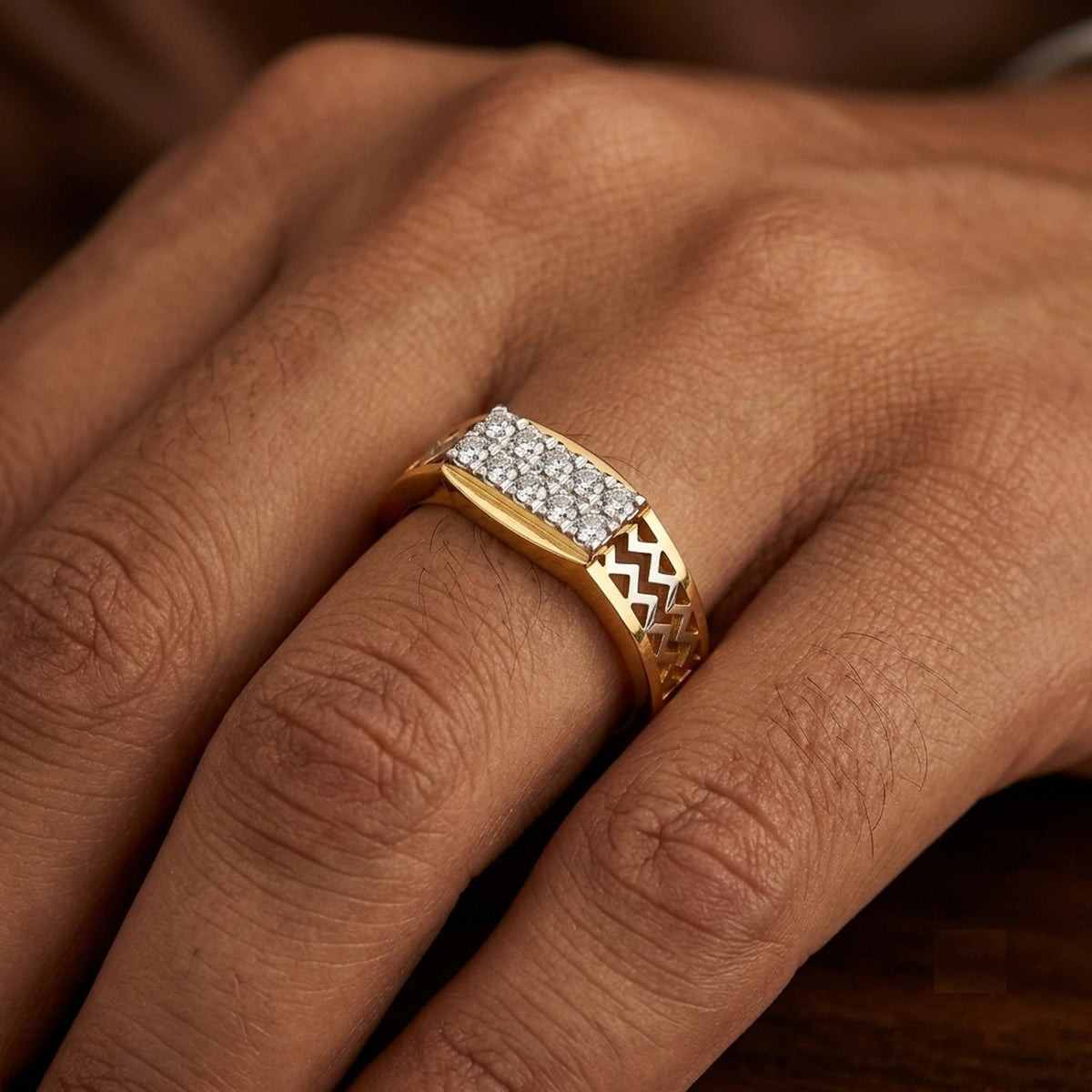 A close-up of a gold ring with a rectangular pavé diamond top and a chevron-patterned band, worn on a person's finger.