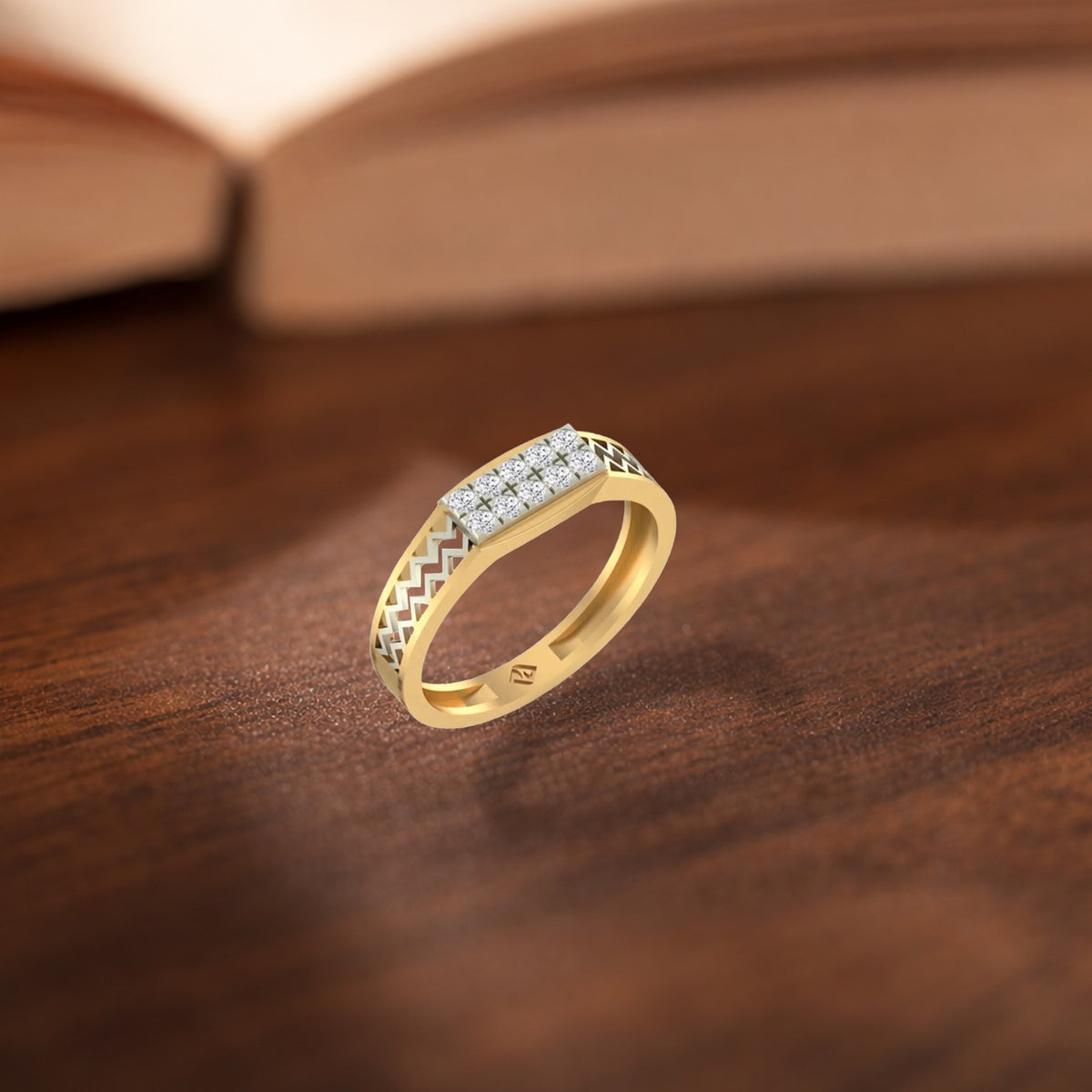 A yellow gold ring with a textured chevron pattern, an open book blurred in the background.