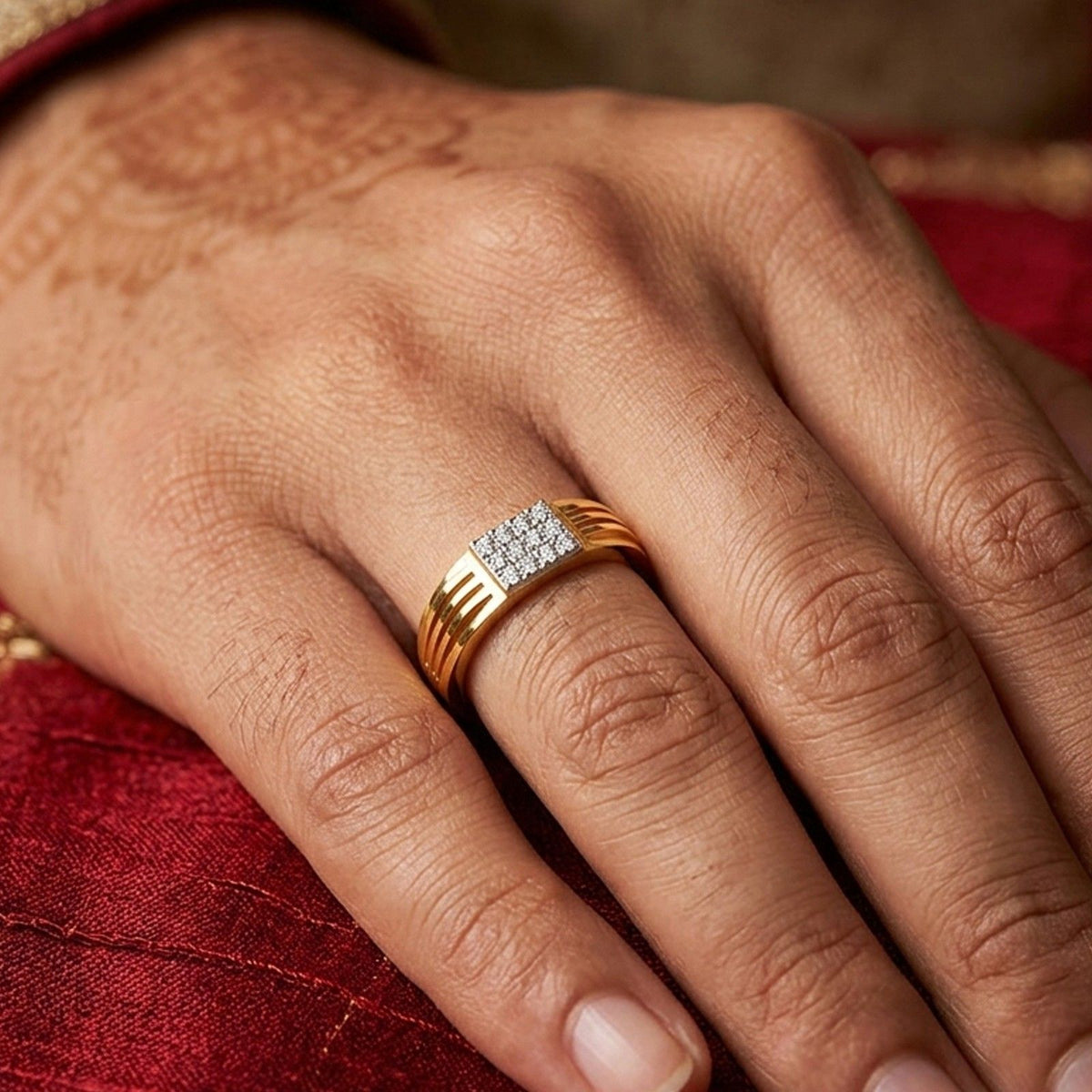 A close-up of a man's hand resting on a wooden surface, wearing a gold ring with a square-cut diamond center stone.