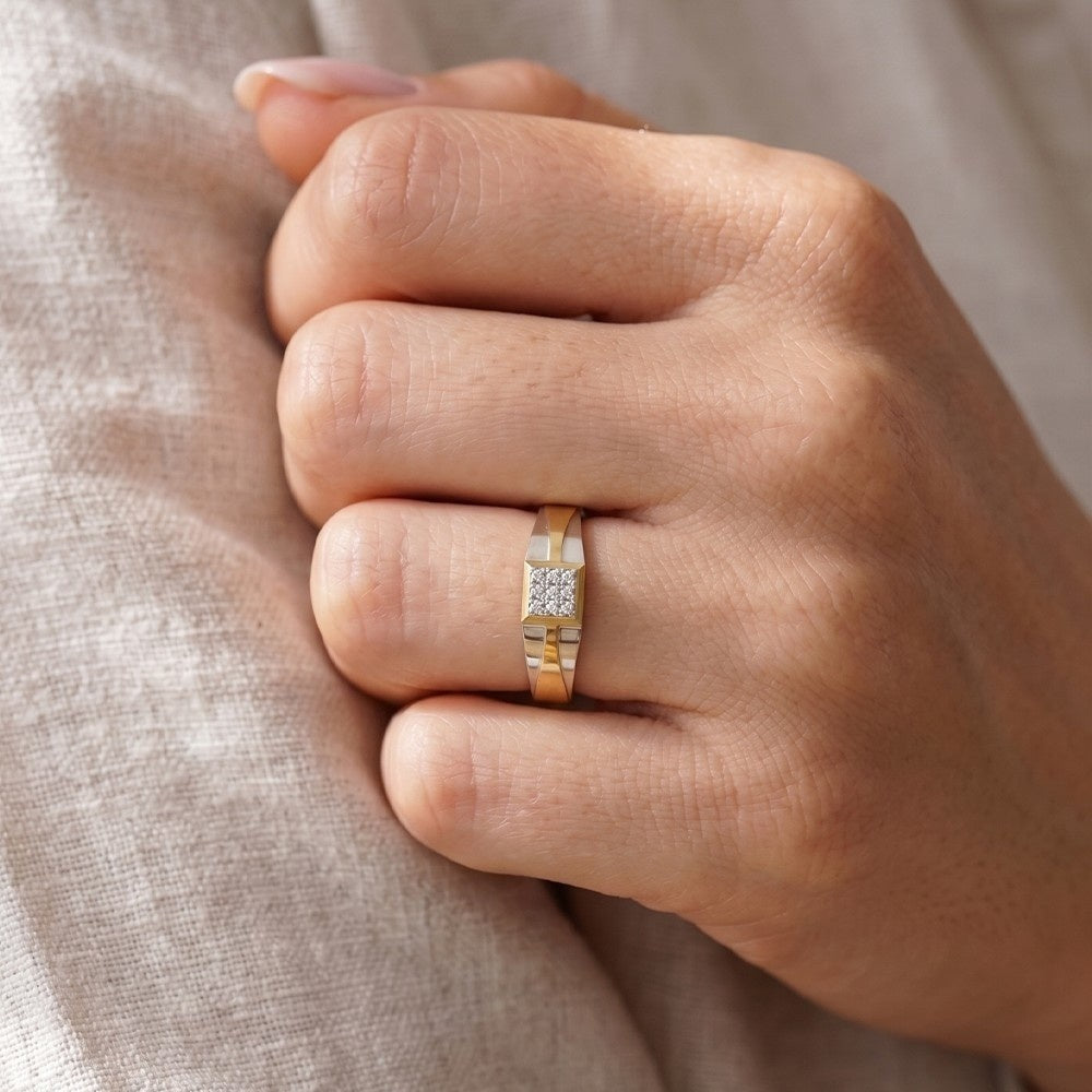 Hand wearing a gold ring with small diamonds on a beige fabric background.