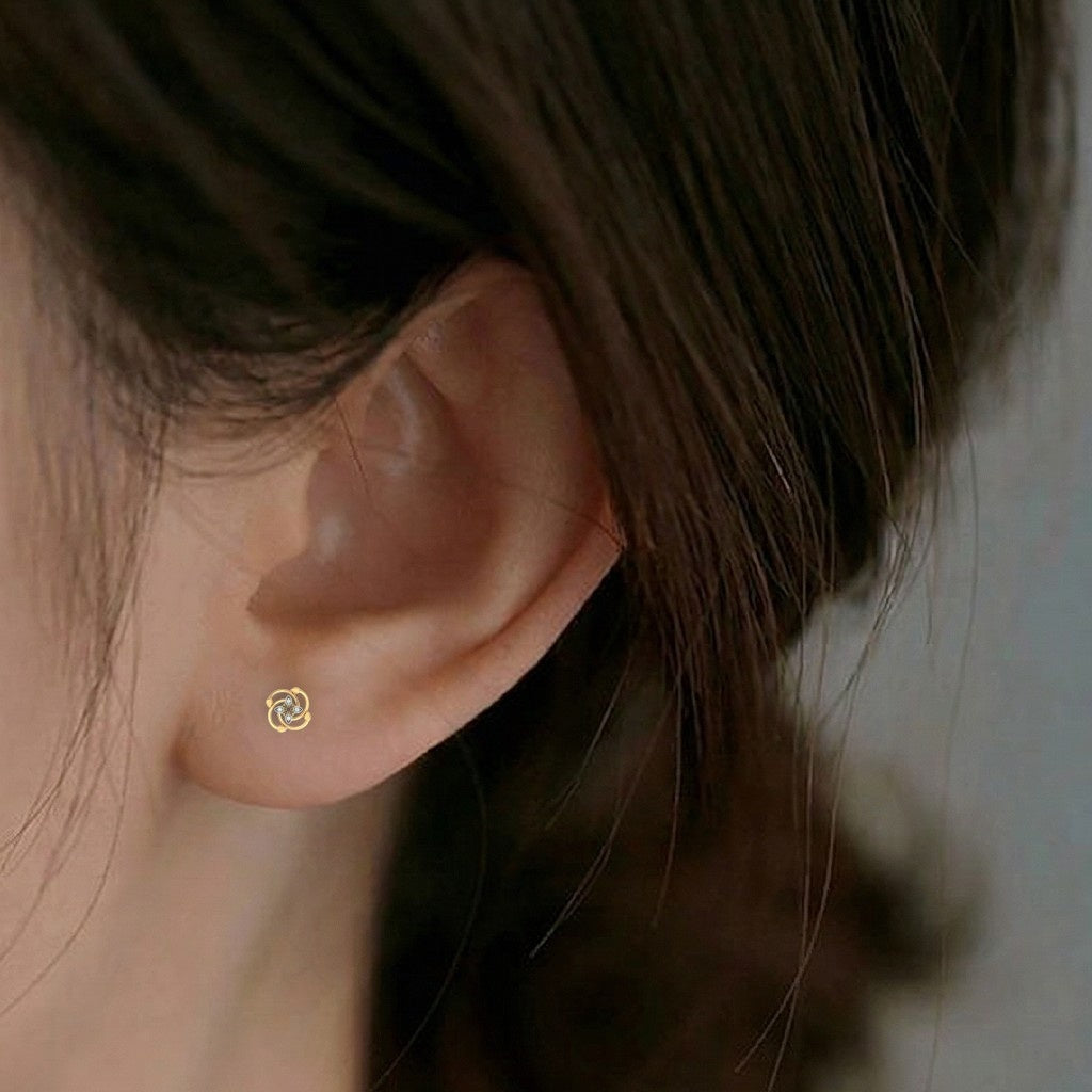 A close-up of a person's ear wearing a small gold stud earring with a floral design.