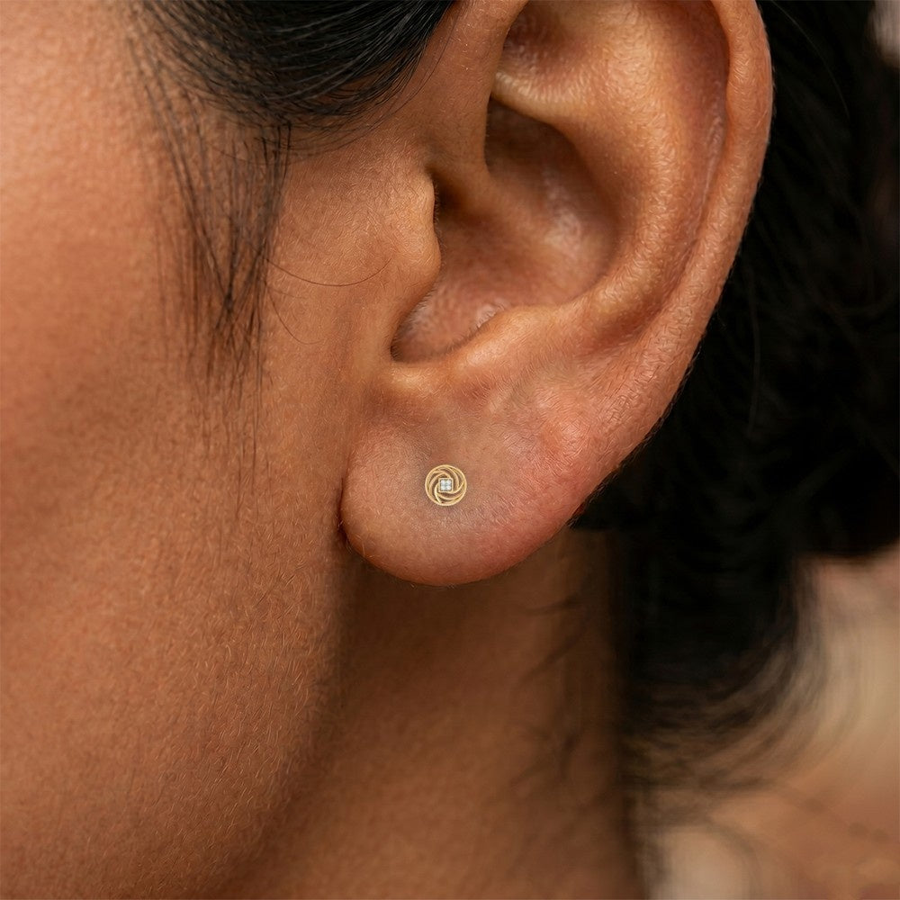 Close-up shot of a gold swirl stud earrings with a diamond center.