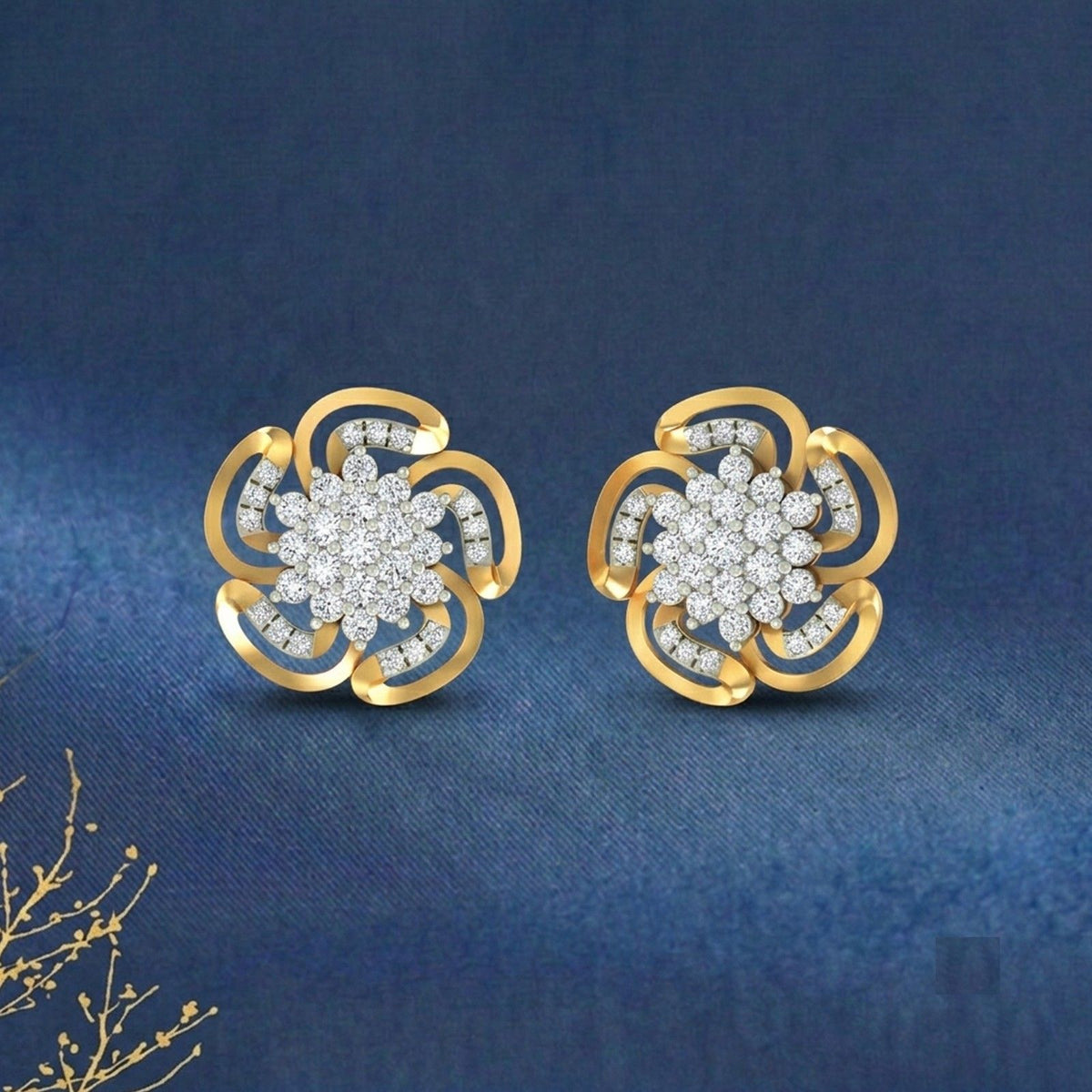 A pair of gold flower-shaped stud earrings, displayed on a textured dark blue fabric background.