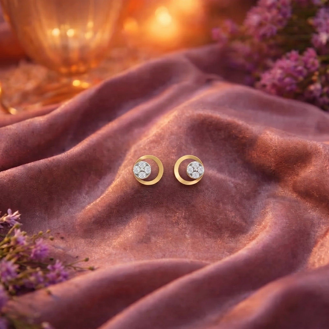 Gold and diamond earrings on a soft fabric background with flowers.