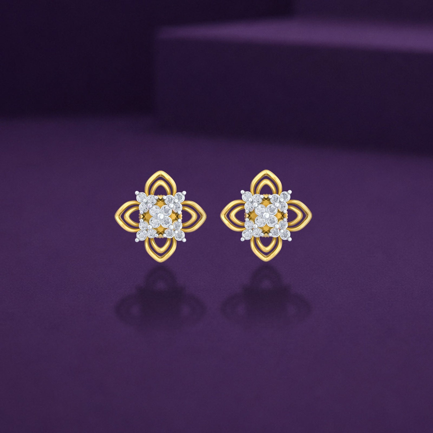 A pair of gold and diamond floral stud earrings resting on a dark purple surface.
