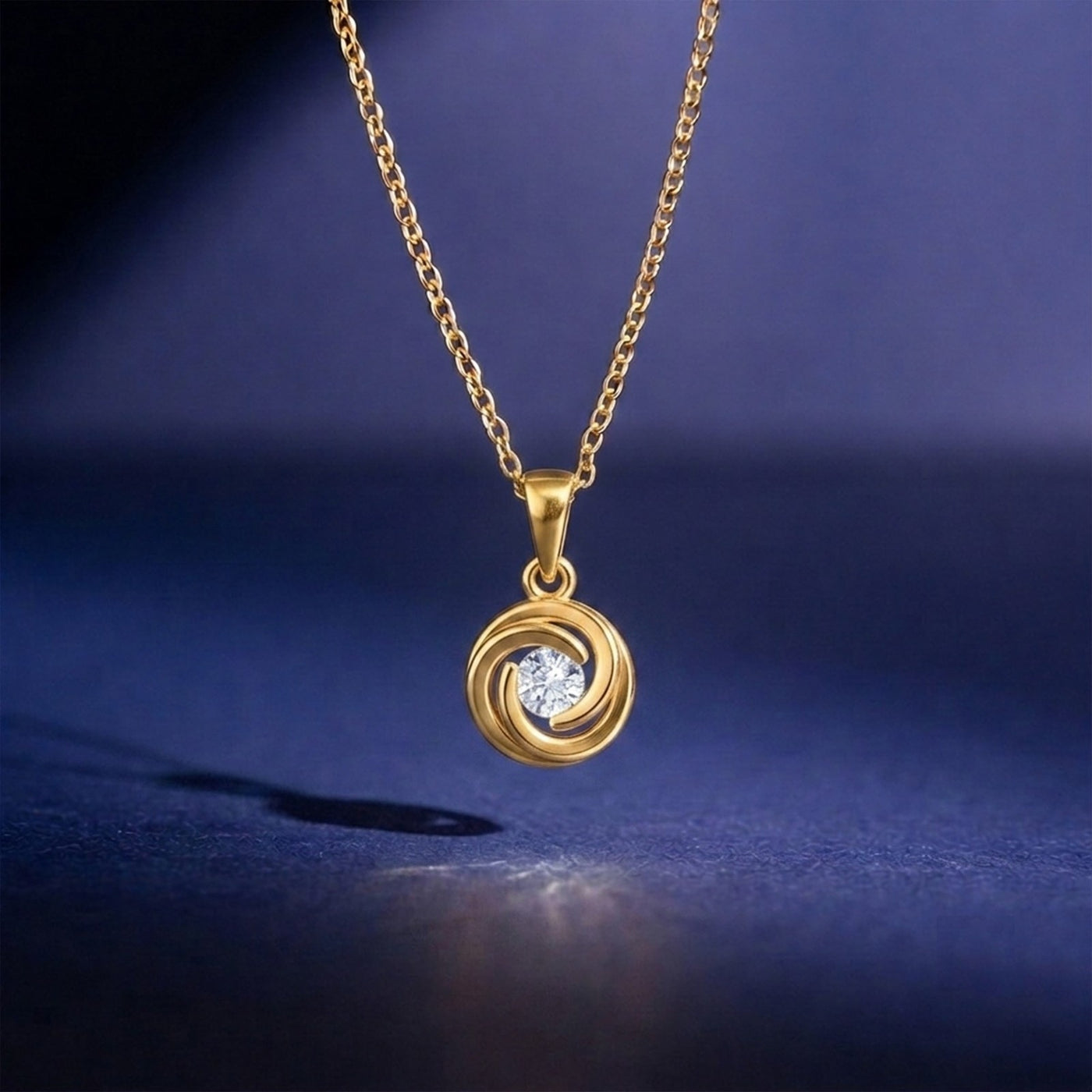 A gold pendant with a circular swirl  featuring a clear central gemstone, displayed against a dark blue background.