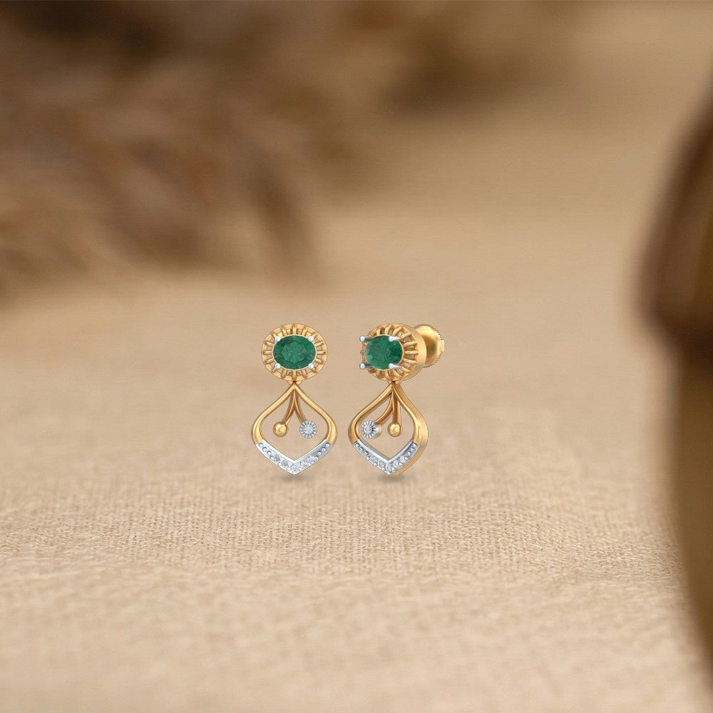 Gold and diamond earrings with emerald gemstones on a beige fabric background.