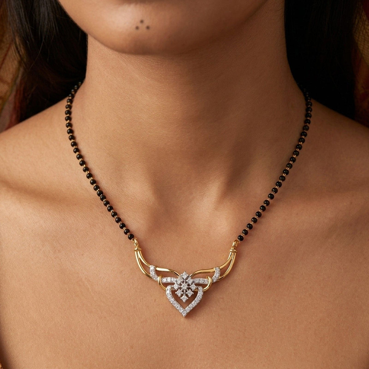 A close-up of a woman's neck and chest wearing a black beaded mangalsutra with a gold and diamond heart-shaped.