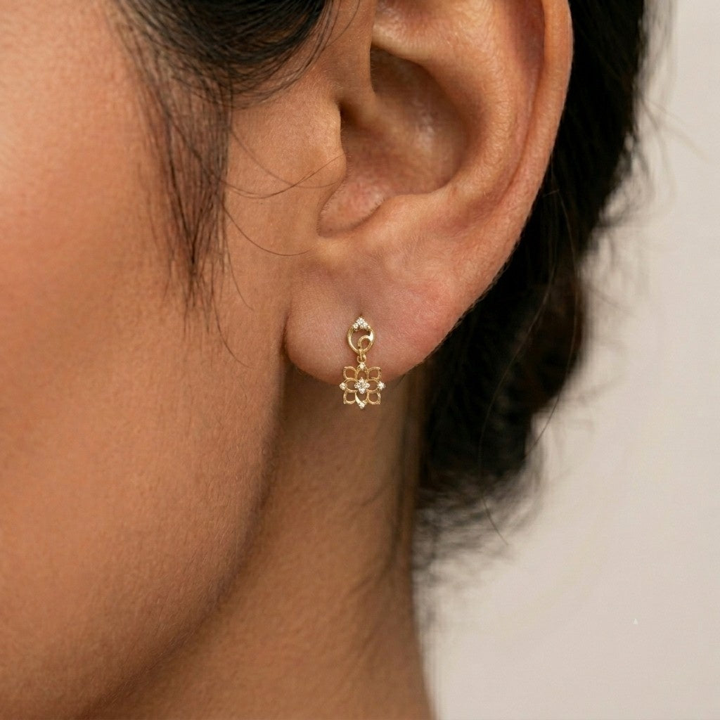 A close-up of a person's ear wearing a gold and diamond flower-shaped drop earring.