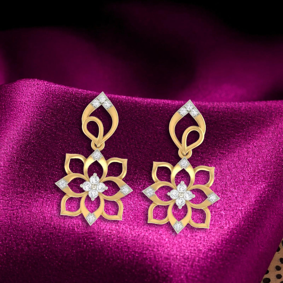 A pair of gold and diamond floral earrings, displayed on a draped magenta satin fabric.