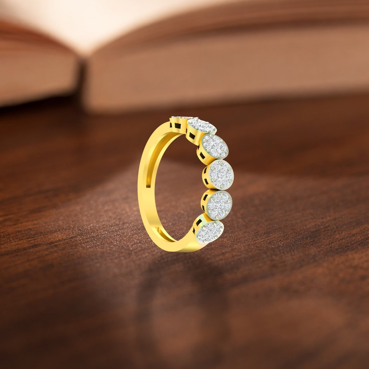 A gold ring with five round-cut, displayed on a dark wooden surface with a blurred book in the background.