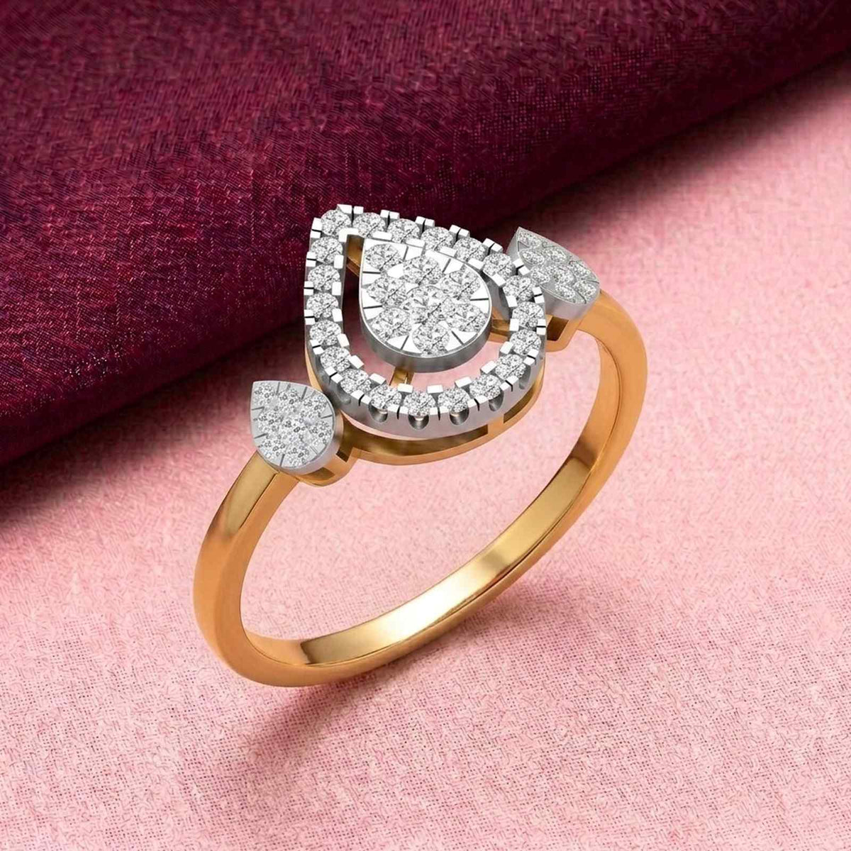 A gold ring with a teardrop-shaped diamond cluster centerpiece, displayed on a pink textured surface.