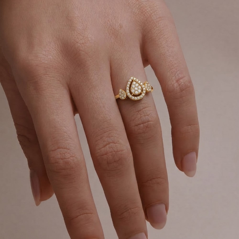 A gold ring with a teardrop-shaped cluster, worn on a person's finger against a soft beige background.