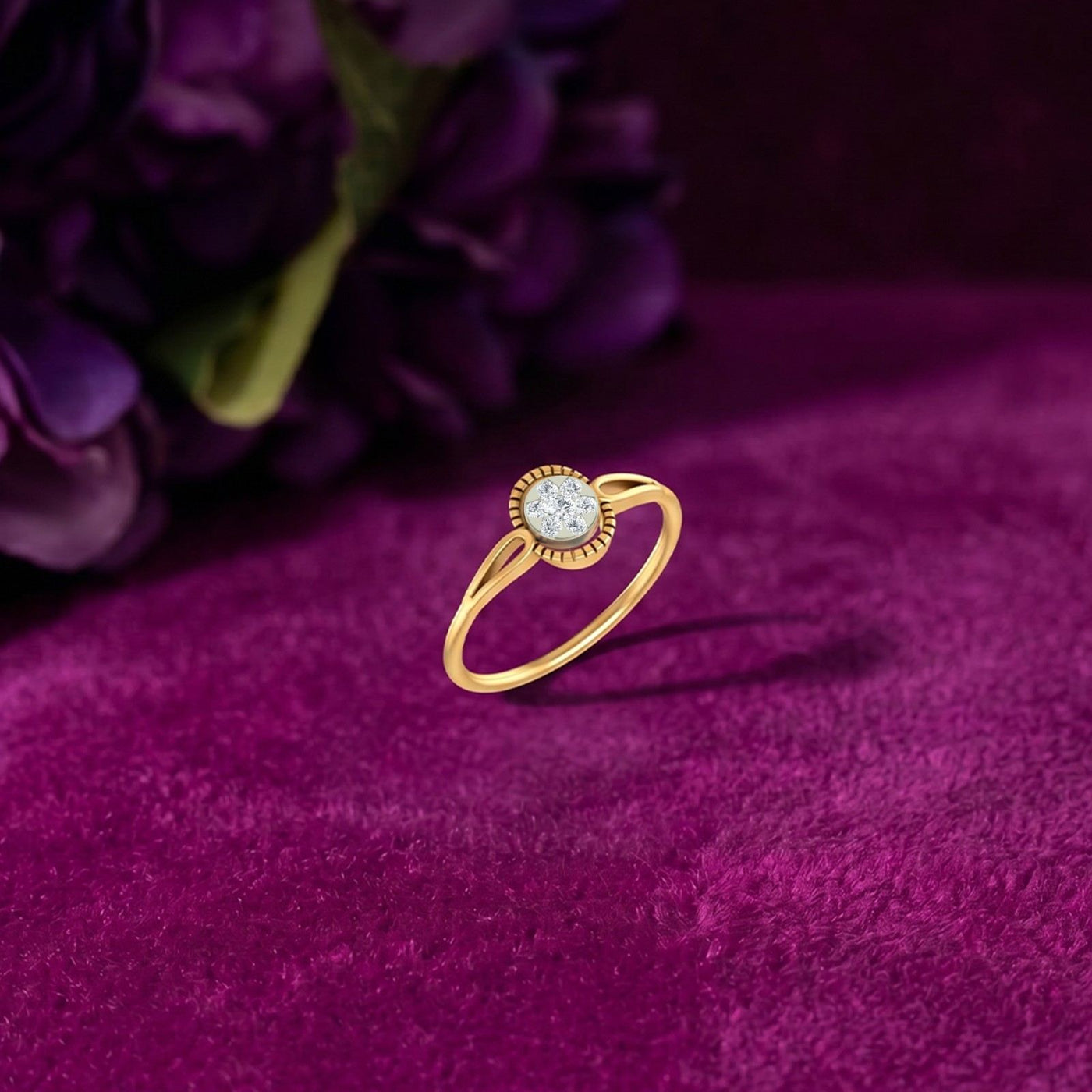 A gold and diamond ring, resting on a deep magenta velvet surface with blurred purple flowers in the background.