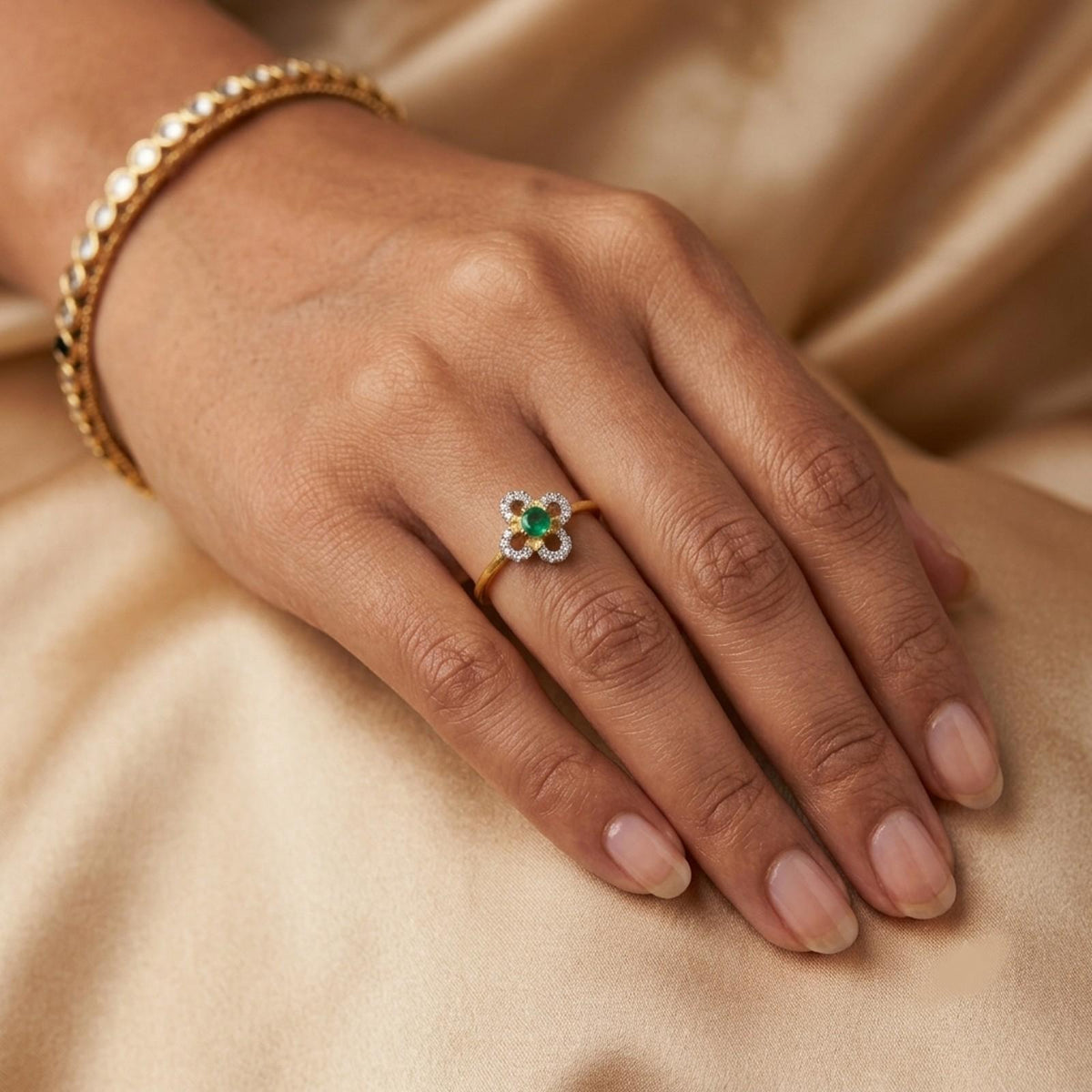Close-up shot of a gold and diamond with floral-design and center emerald gemstone setting ring.