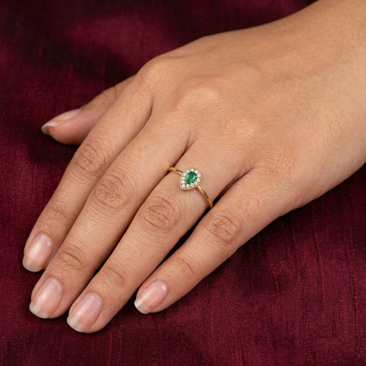 Close-up shot of a gold and diamond with teardrop emerald gemstone setting ring.