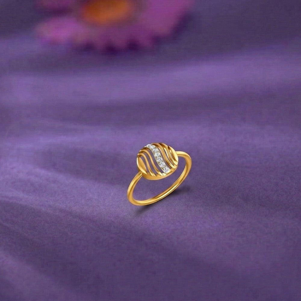 A gold ring with a textured, wavy circular center and a row of small clear stones, resting on a purple fabric surface.