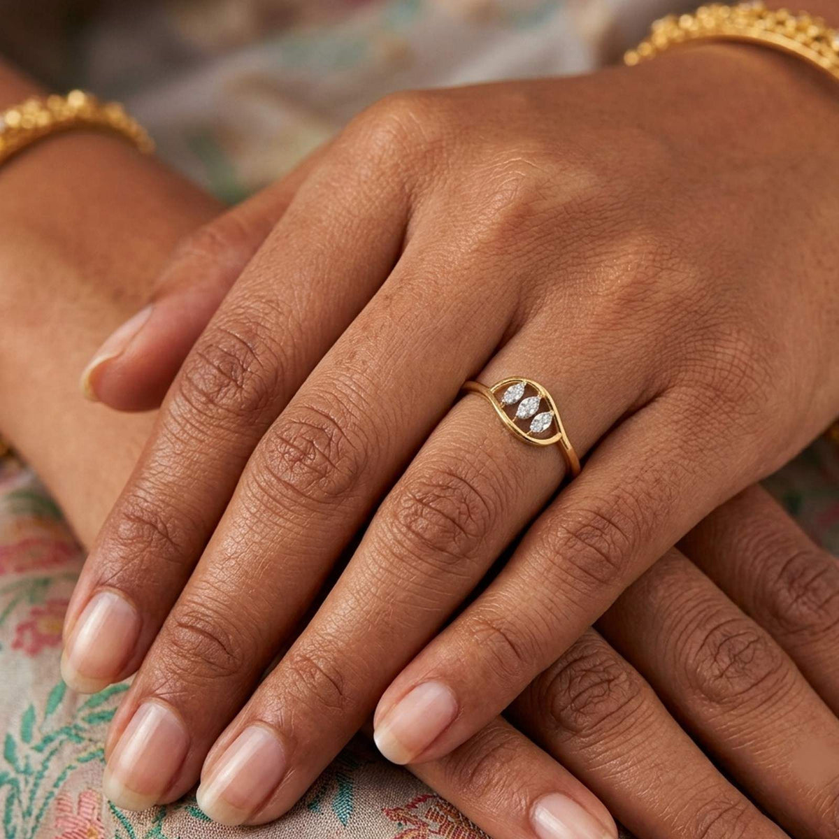 A close-up of a person's hands wearing a gold ring, set against a soft floral fabric background.