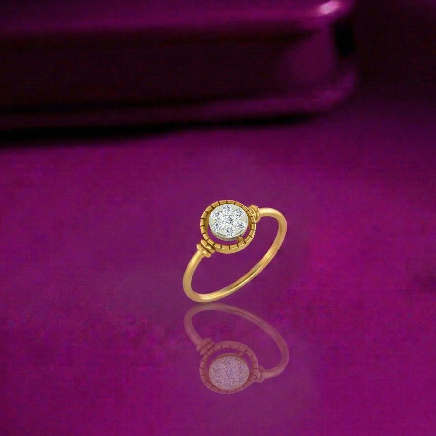 A gold and diamond ring with halo design, displayed on a reflective magenta surface with a blurred purple background.