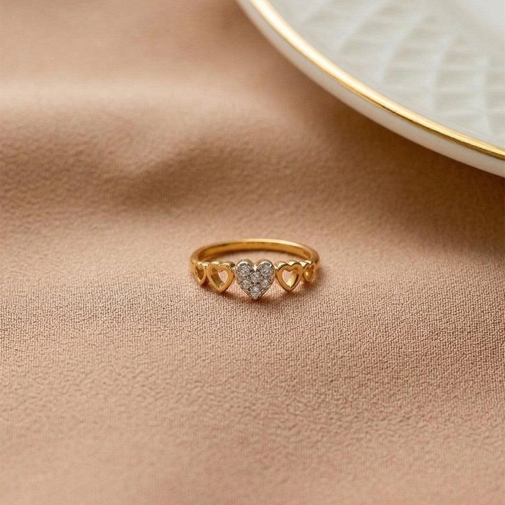 A delicate gold ring featuring three interlocking heart shapes, on a textured beige fabric surface.