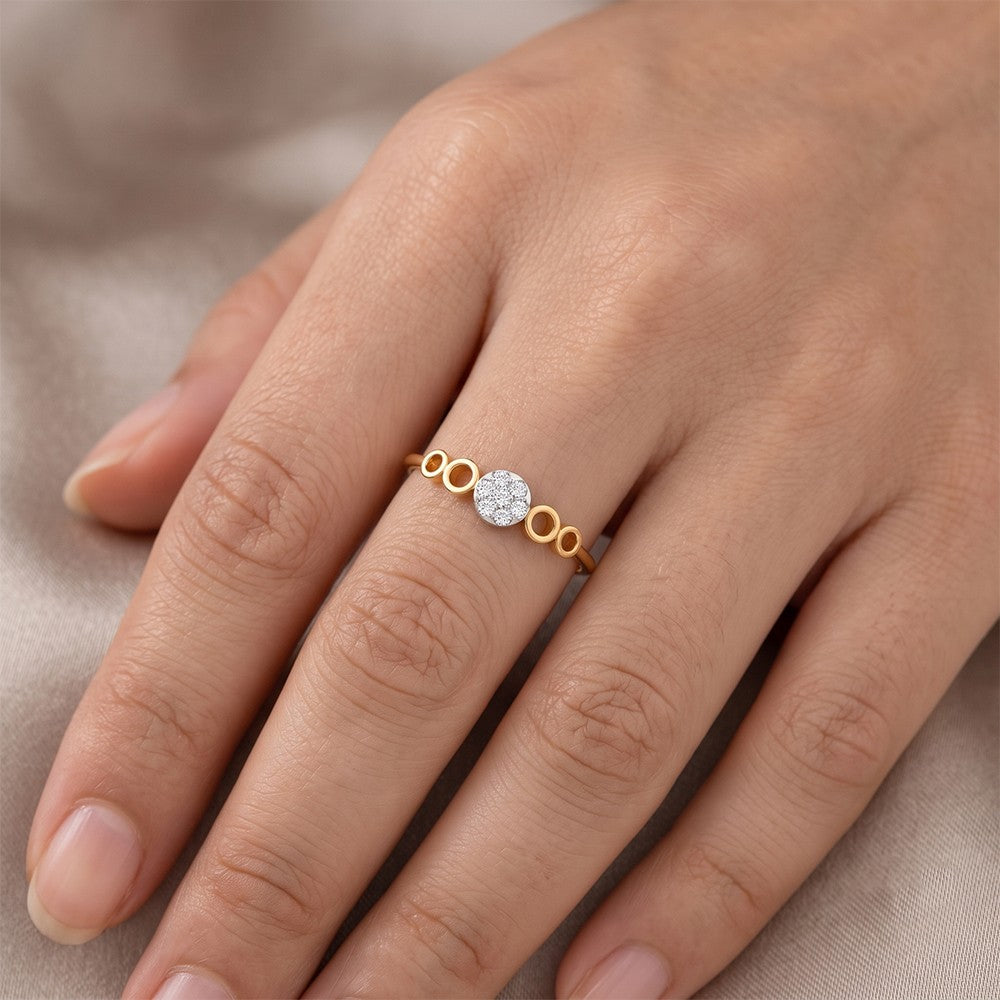 A delicate gold and diamond ring with a central round cluster ring, shown worn on a person's finger against a soft beige fabric background.