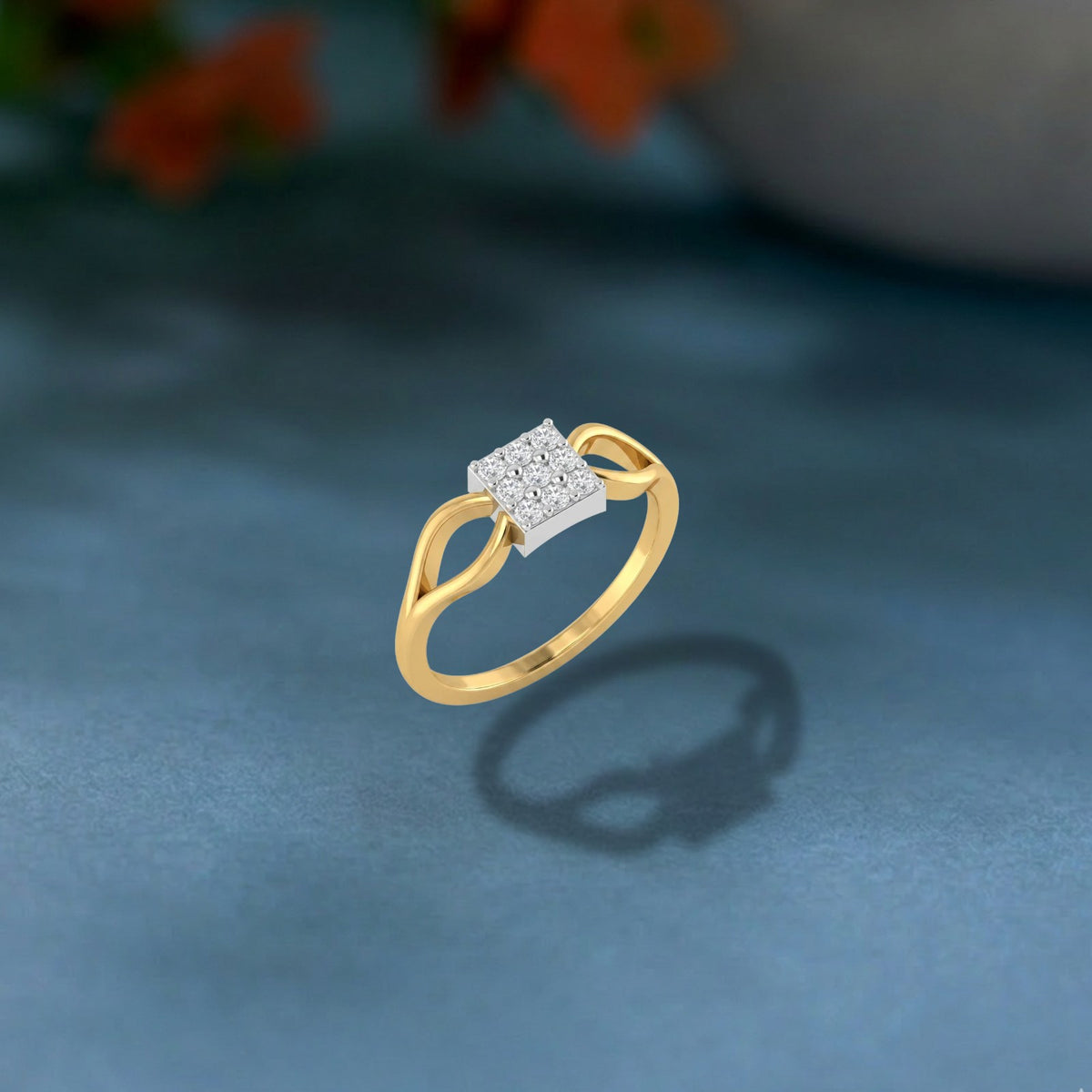 A gold ring with a square-cut diamond center, displayed on a textured blue surface with a soft-focus background.