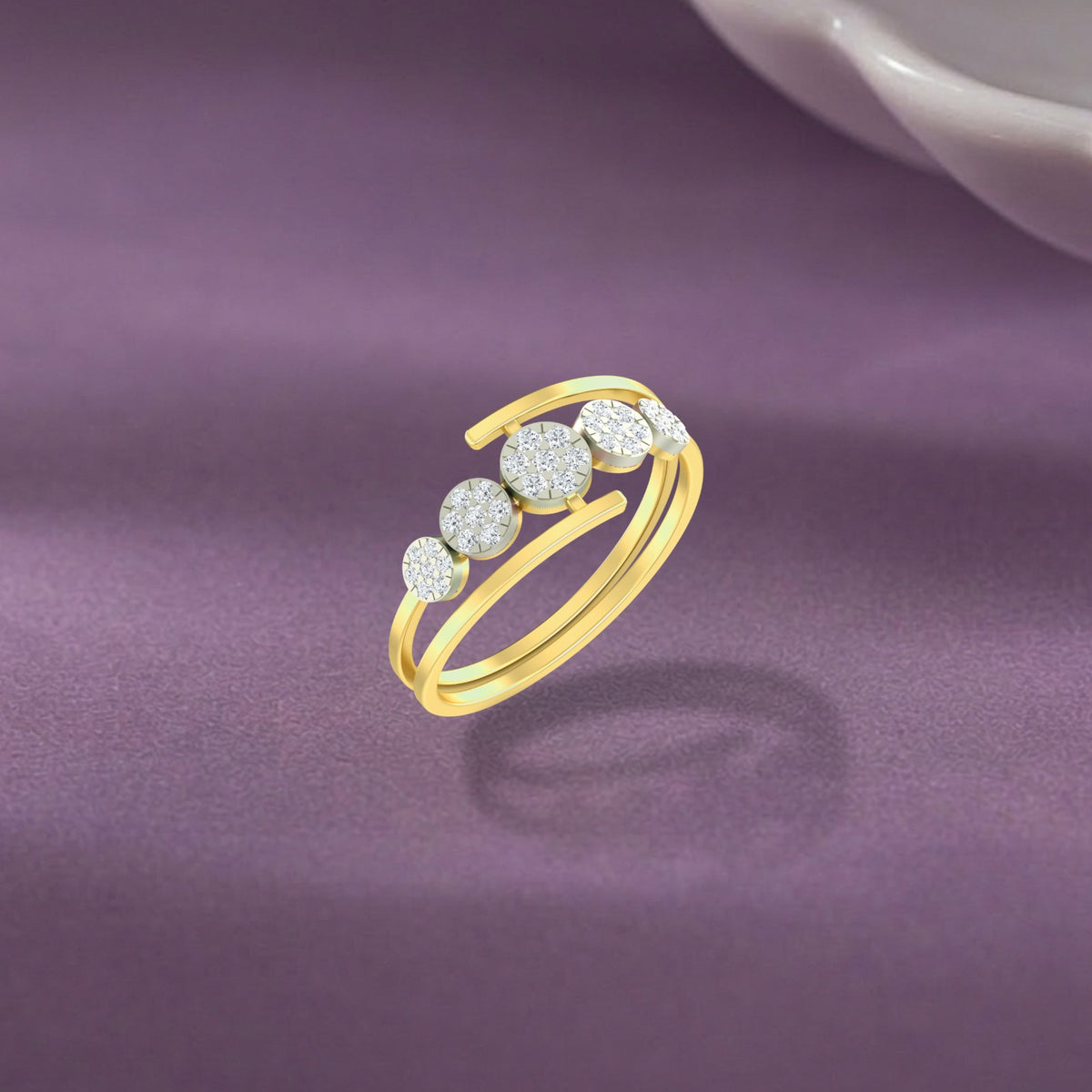 A gold ring with four round-cut set in a curved, displayed on a textured purple surface.
