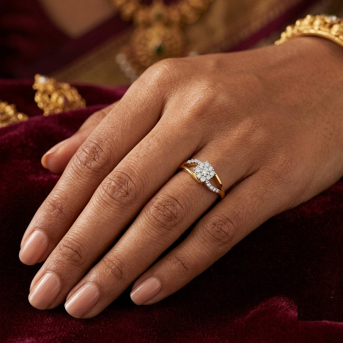 A close-up of a hand wearing a gold ring with a pavé diamond setting, resting on a deep burgundy velvet surface.