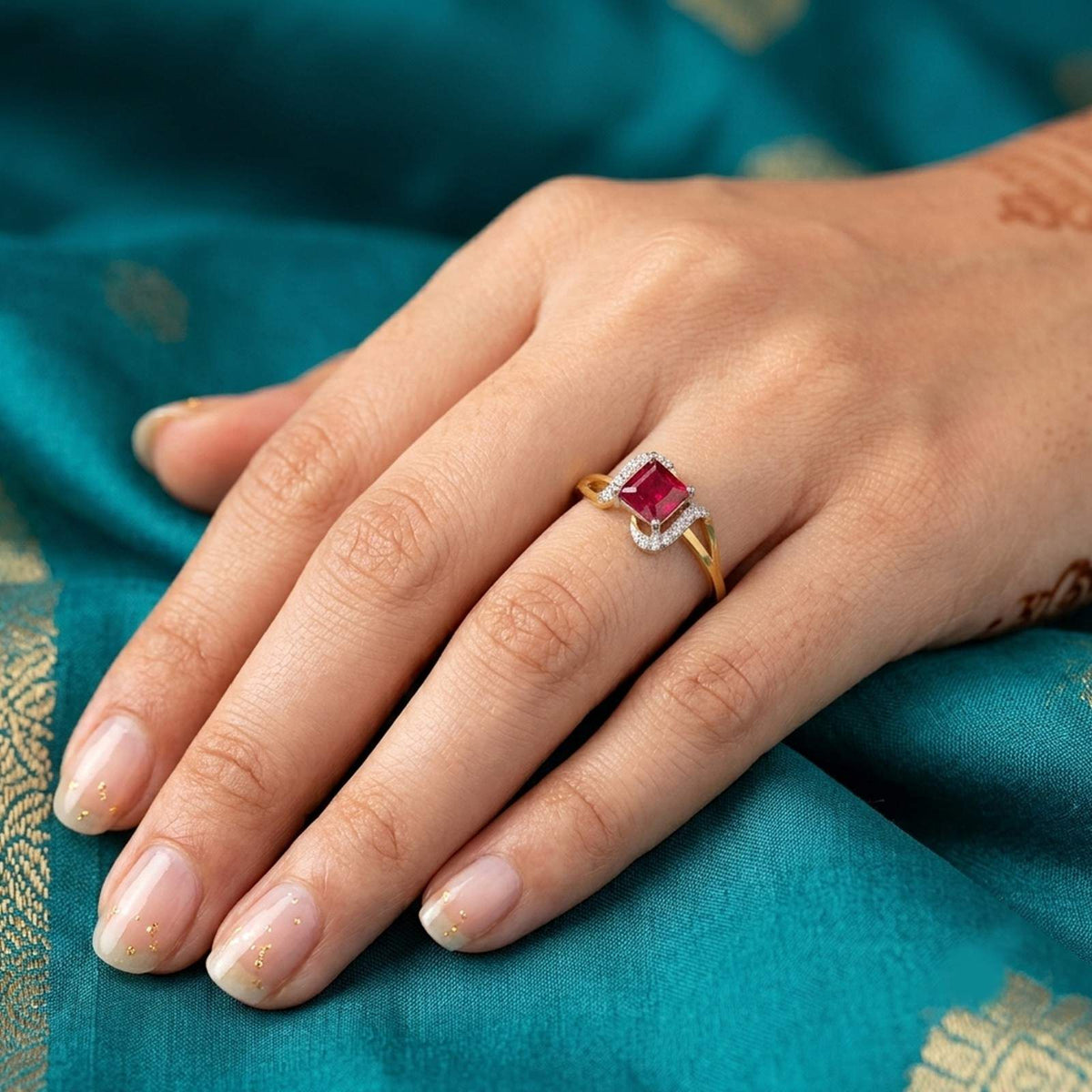 A close-up of a hand wearing a gold ring with a rectangular red gemstone ring.