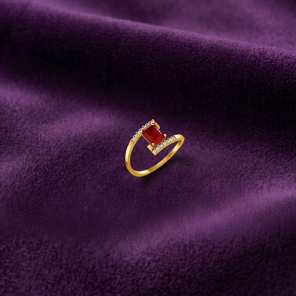 A gold ring with a rectangular ruby gemstone, displayed on a textured purple fabric background.