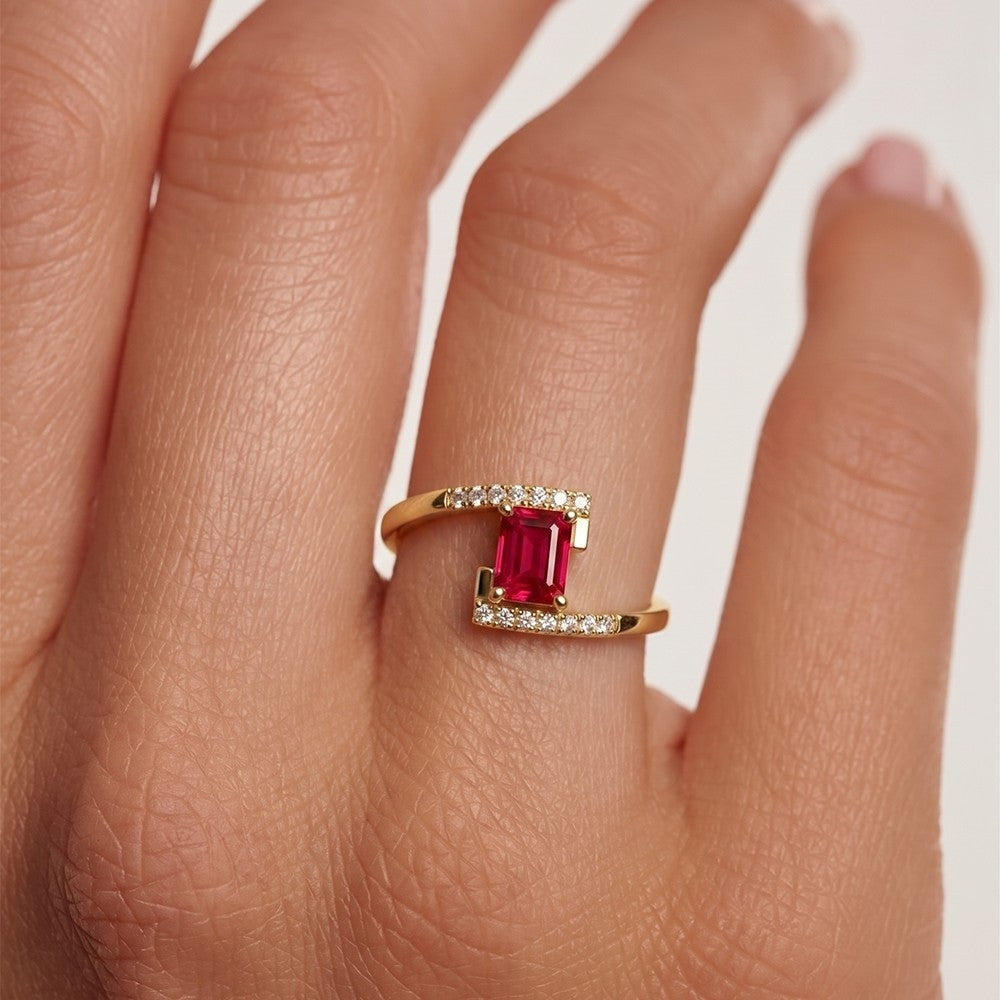 Gold ring with a red gemstone on a person's finger against a white background
