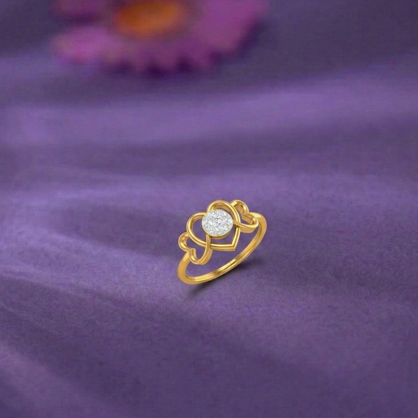 A gold ring featuring a heart-shaped design with a central cluster, resting on a purple fabric background.