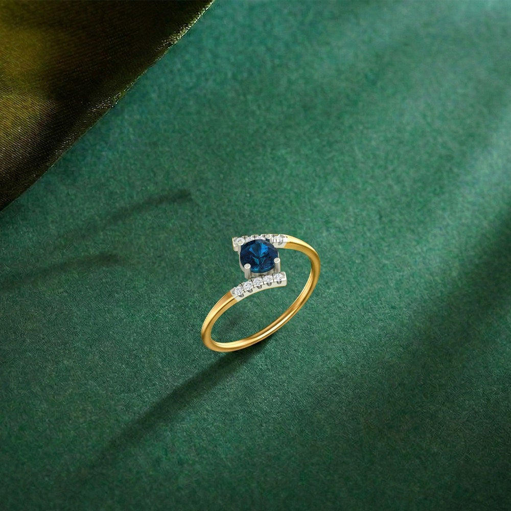 A gold ring with a square-cut blue gemstone, displayed on a textured dark green surface.