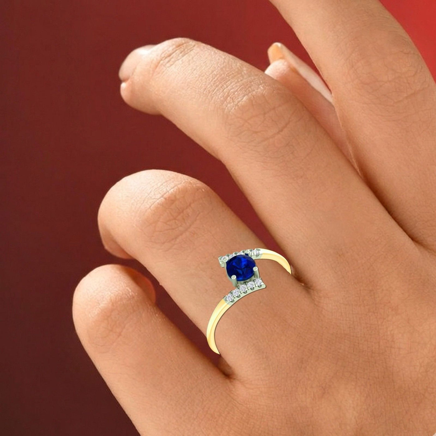 Gold ring with a blue gemstone on a hand against a red background