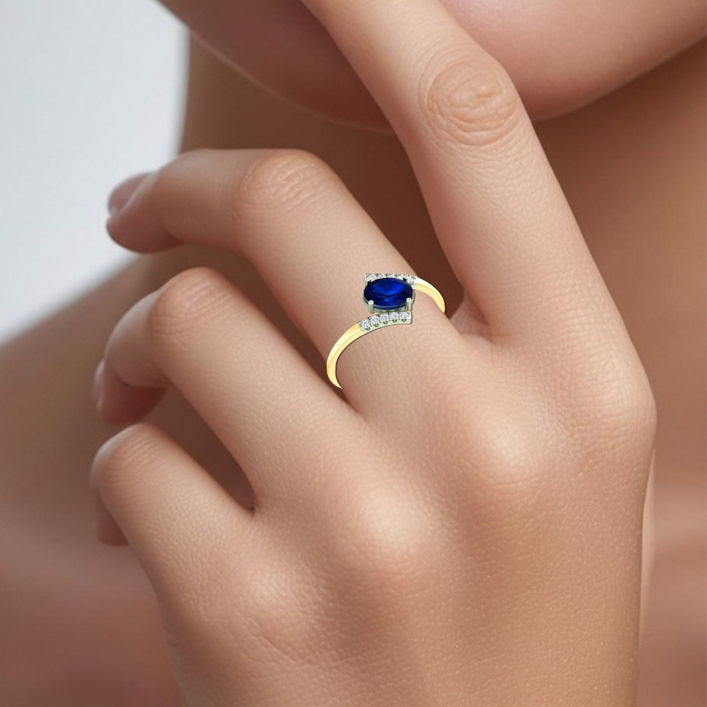 A close-up of a hand wearing a yellow gold ring with a deep blue oval gemstone and small clear accent stones.