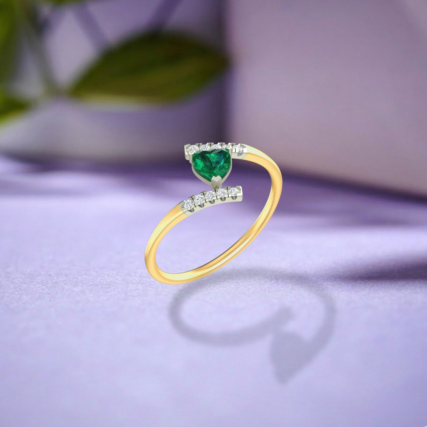 Gold and diamond ring with a heart-shaped emerald on a purple surface.